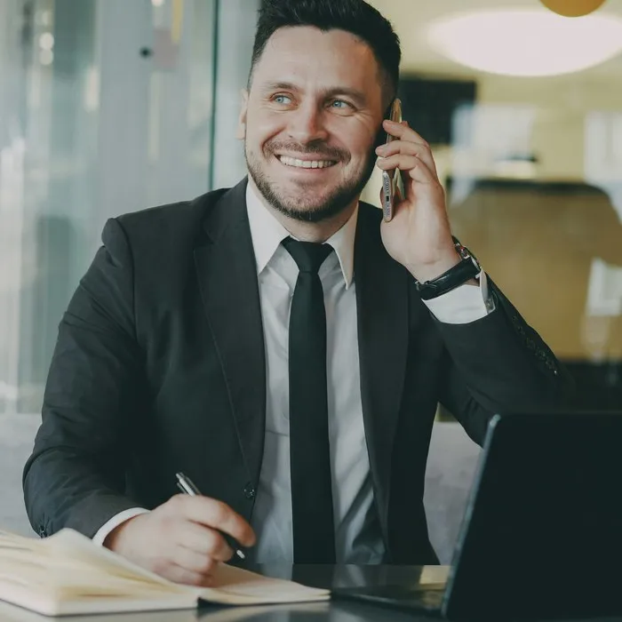 Usměvavý muž v obleku telefonuje u svého stolu
